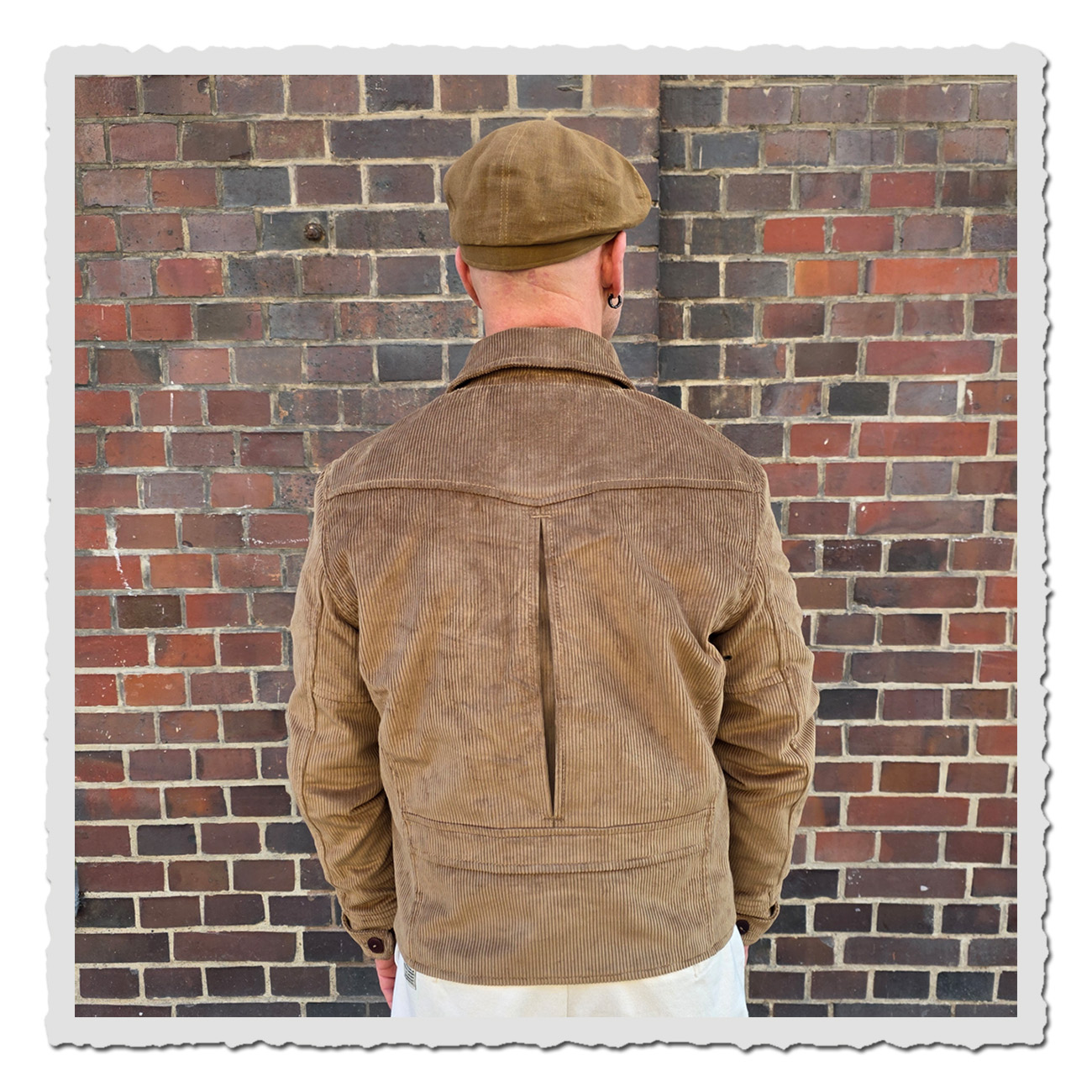 Mann vor Ziegelwand trägt Pike Brothers 1932 Roadster Jacket Light Brass Cord – hier Rückenansicht